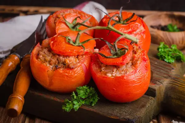 Quatre tomates farcies appétissantes, garnies d'une farce savoureuse, reposent sur une planche en bois rustique.
