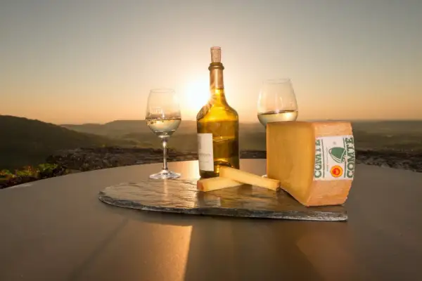 Un coucher de soleil sur le Jura, avec un verre de vin jaune, une bouteille et du fromage Comté. Qu'est-ce que le vin jaune ? C'est un vin du Jura, unique et savoureux.