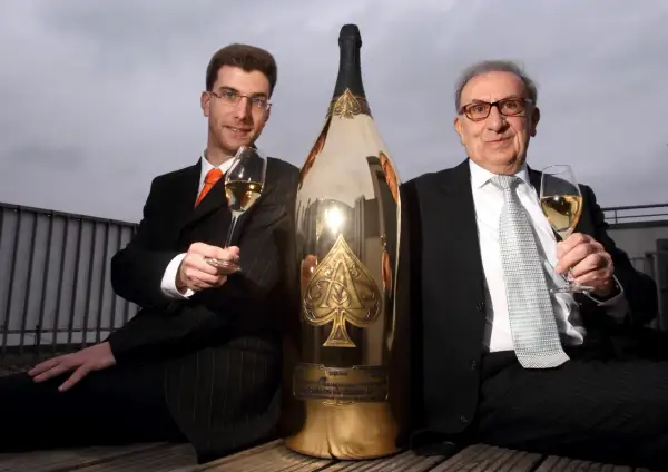Deux hommes en costume célèbrent avec une gigantesque bouteille de champagne dorée, une véritable bouteille Midas.