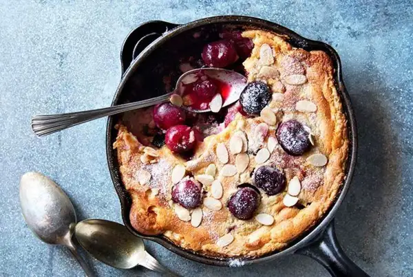 Clafoutis aux cerises dans une poêle, saupoudré de sucre glace et d'amandes effilées. Une recette clafoutis facile et gourmande.