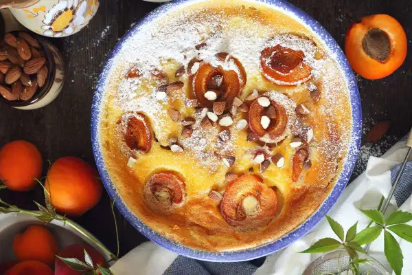 Un délicieux flan aux abricots, saupoudré de sucre glace et parsemé d'amandes concassées, prêt à être dégusté.